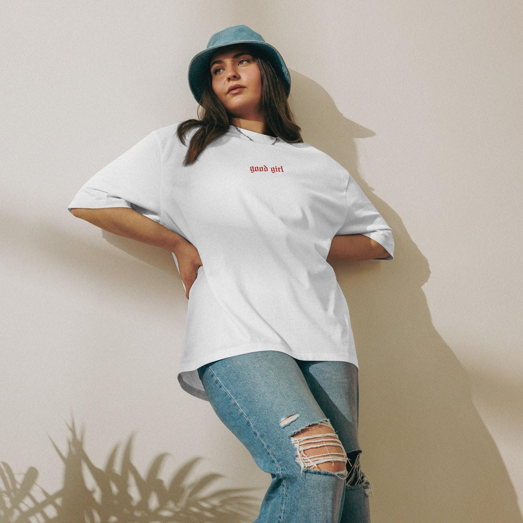 Woman wearing embroidered good girl tee in white with red text paired with ripped jeans and a blue bucket hat